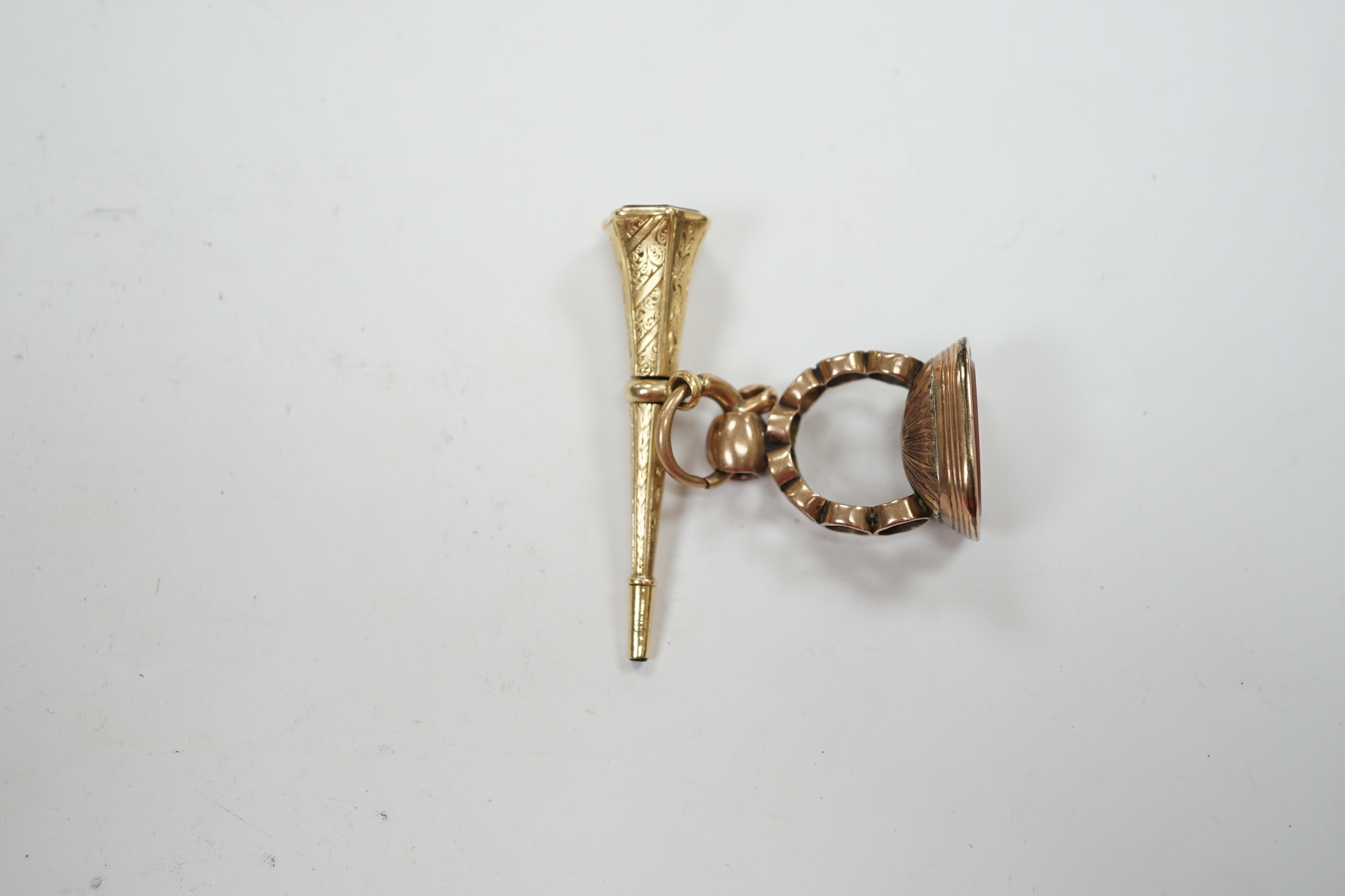 A 19th century engraved yellow metal overlaid and carnelian set trumpet shaped watch key, the matrix carved with crest and initial, 51mm, together with a 19th century gold plated and carnelian set fob.